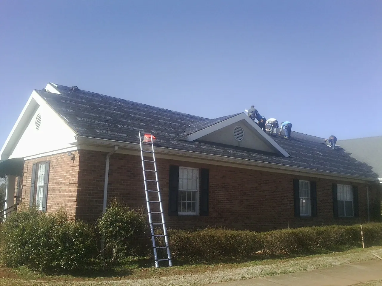 Crew tearing shingles off a brick ranch roof with a ladder set — Metal Roof Repair work by our crew in Orlando