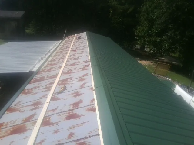 Old rusted panels beside newly installed green metal roofing in Orlando