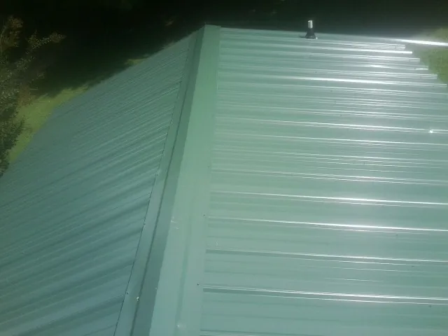 New green metal panels meeting at the ridge of a roof — Flat Roof Repair work by our crew in Orlando