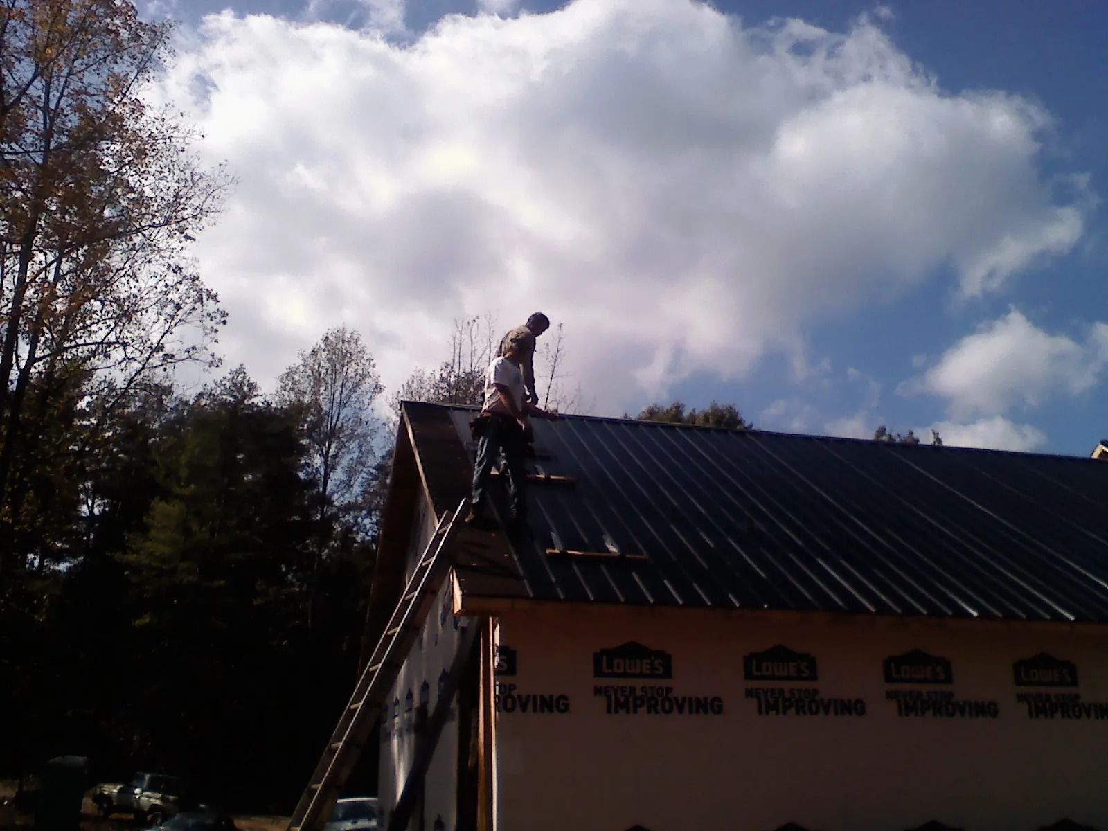 Roofer fastening dark metal panels high against a cloudy sky, from a Roof Inspection job in Orlando